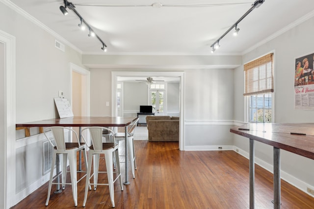 dining room featuring dark wood-type flooring, track lighting, and crown molding