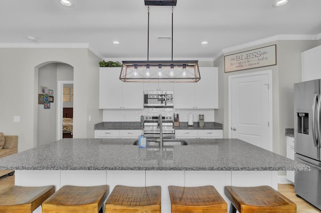 kitchen with an island with sink, stainless steel appliances, sink, decorative light fixtures, and white cabinetry