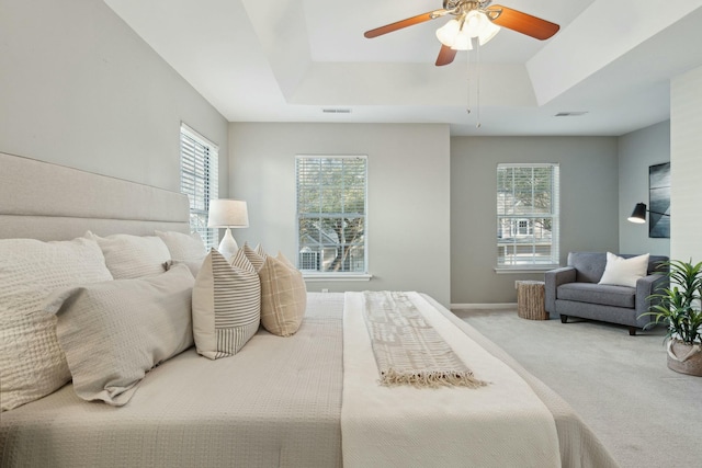 carpeted bedroom featuring a tray ceiling, visible vents, ceiling fan, and baseboards