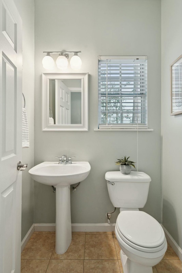 half bathroom with baseboards, toilet, and tile patterned floors