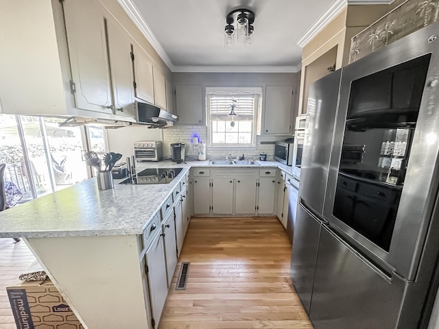 kitchen featuring sink, ornamental molding, appliances with stainless steel finishes, light hardwood / wood-style floors, and decorative backsplash