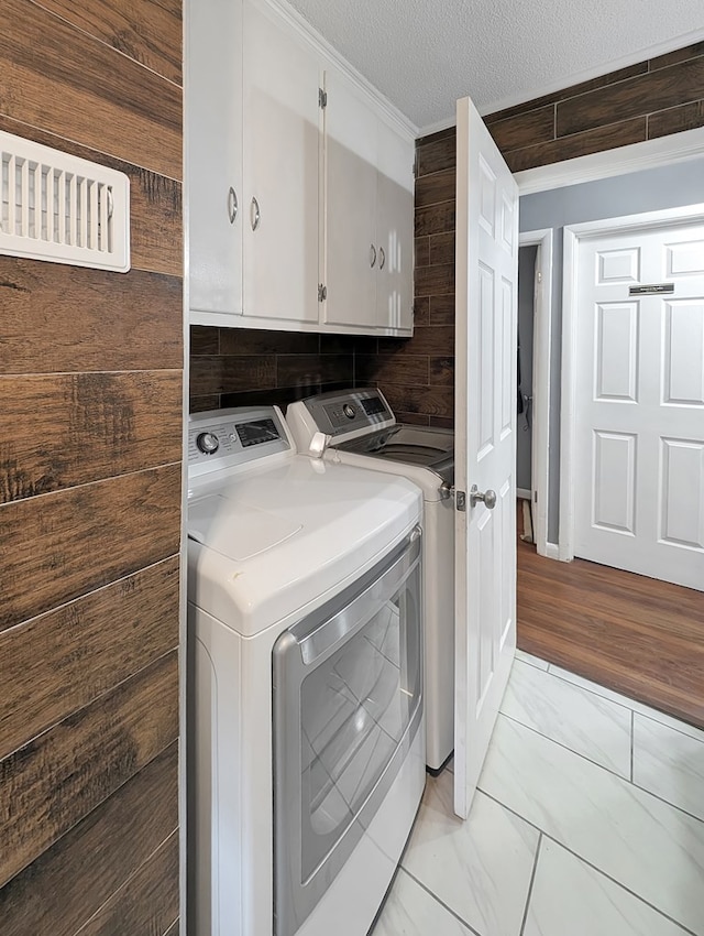 laundry area featuring cabinets, a textured ceiling, separate washer and dryer, and light hardwood / wood-style flooring