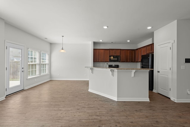 kitchen with hardwood / wood-style floors, hanging light fixtures, a breakfast bar area, black appliances, and sink