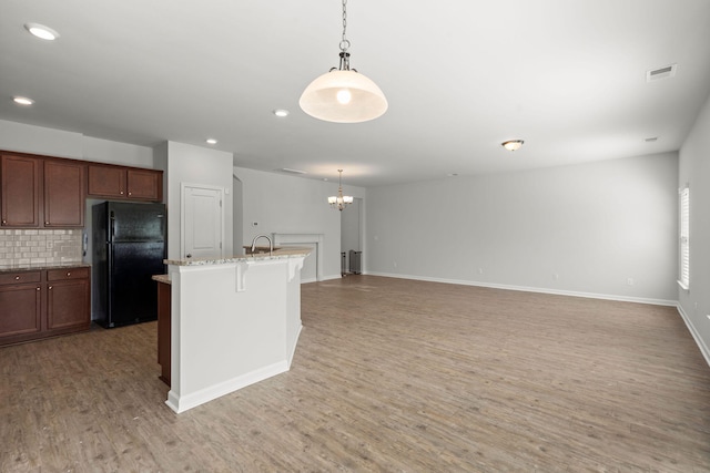 kitchen featuring a kitchen bar, black fridge, decorative backsplash, light hardwood / wood-style flooring, and a kitchen island with sink