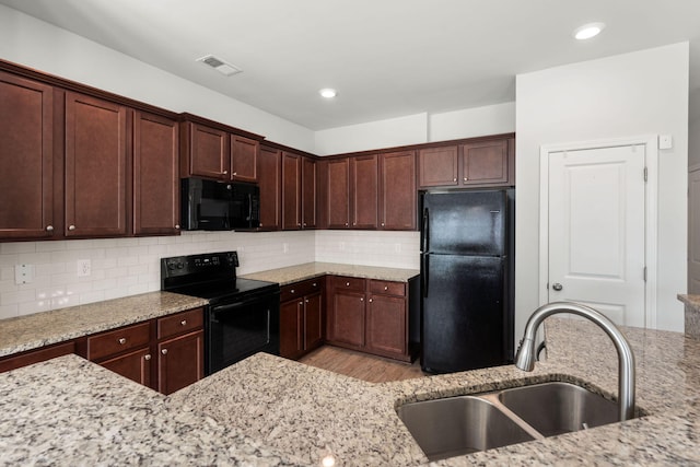 kitchen featuring light stone countertops, black appliances, sink, and backsplash