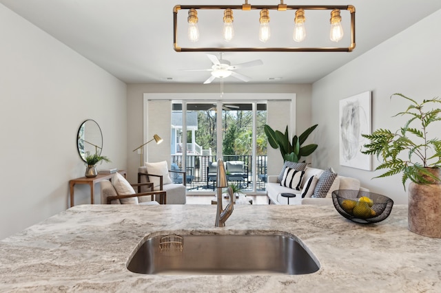 kitchen with light stone counters, a ceiling fan, and a sink