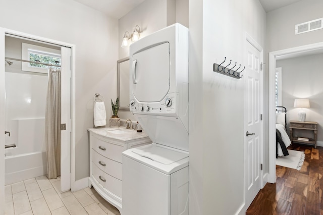 clothes washing area featuring light wood finished floors, visible vents, laundry area, stacked washer / drying machine, and a sink