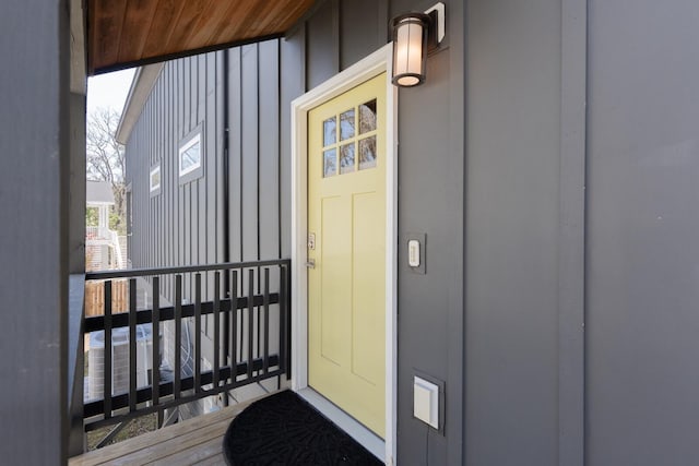 view of exterior entry with a balcony, central AC unit, and board and batten siding