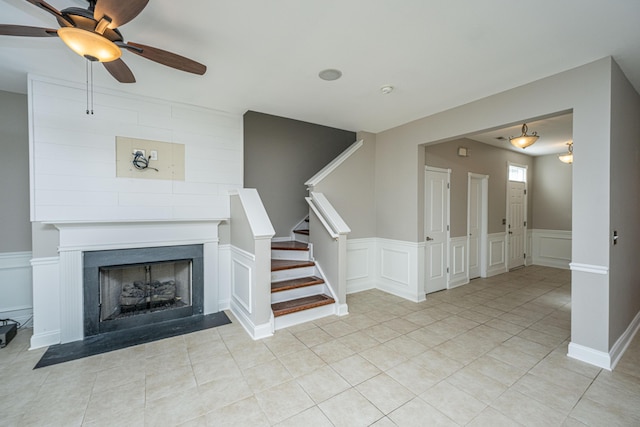 unfurnished living room featuring a large fireplace, stairs, light tile patterned floors, and a decorative wall