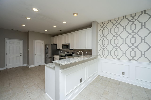 kitchen featuring white cabinets, appliances with stainless steel finishes, light stone counters, a peninsula, and recessed lighting