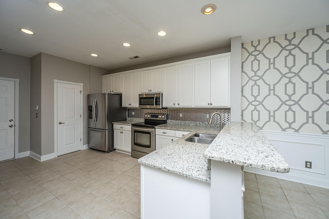 kitchen with white cabinets, a peninsula, light stone countertops, stainless steel appliances, and a sink