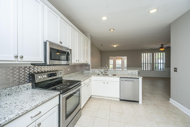 kitchen with appliances with stainless steel finishes, white cabinetry, a sink, light stone countertops, and a peninsula