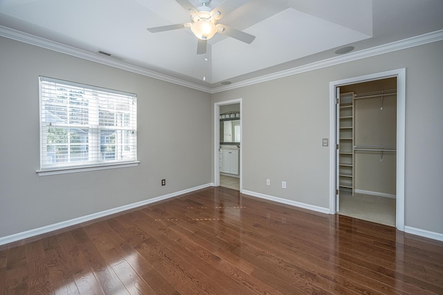 unfurnished bedroom featuring a walk in closet, dark wood-style flooring, crown molding, and baseboards