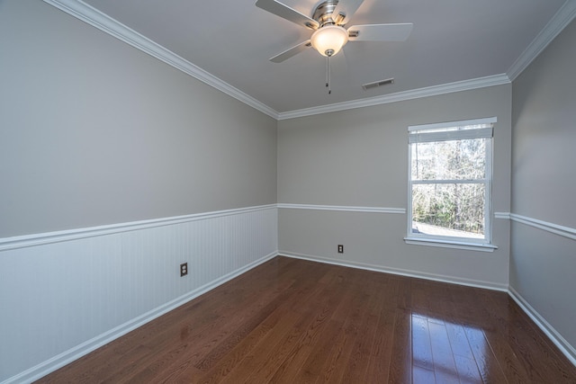 empty room with ceiling fan, dark wood-type flooring, visible vents, baseboards, and ornamental molding