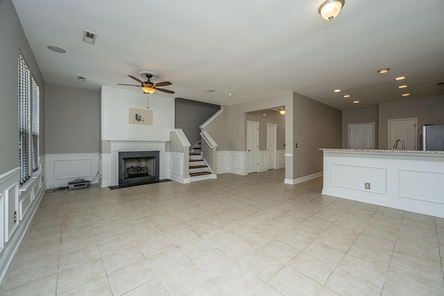 unfurnished living room with stairway, a fireplace with flush hearth, visible vents, and a decorative wall