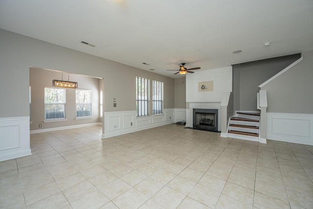 unfurnished living room featuring light tile patterned floors, ceiling fan, a fireplace, and a decorative wall