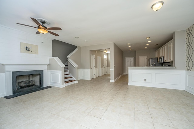 unfurnished living room with stairs, a fireplace with flush hearth, a ceiling fan, and a decorative wall