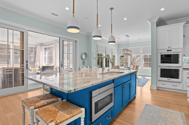 kitchen featuring stainless steel microwave, blue cabinets, crown molding, double oven, and a sink