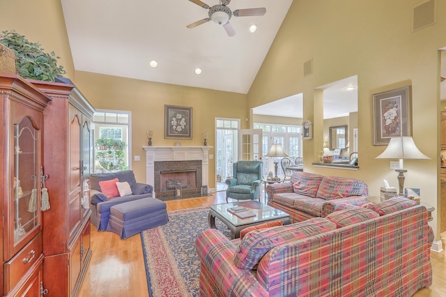 living room featuring light hardwood / wood-style floors, high vaulted ceiling, a premium fireplace, and ceiling fan