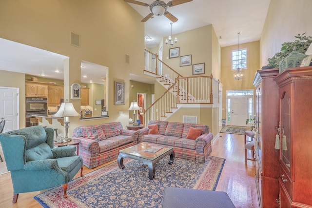 living room featuring light hardwood / wood-style flooring, ceiling fan with notable chandelier, and a towering ceiling