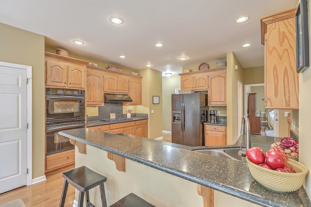 kitchen with appliances with stainless steel finishes, sink, kitchen peninsula, a breakfast bar area, and light hardwood / wood-style flooring