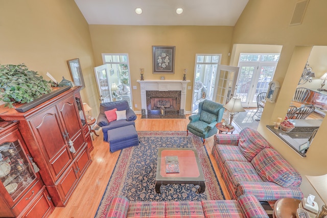 living room featuring a high end fireplace, french doors, high vaulted ceiling, and light hardwood / wood-style floors