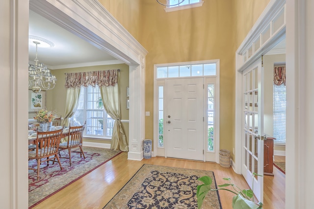 entryway featuring an inviting chandelier, crown molding, a towering ceiling, and light hardwood / wood-style floors