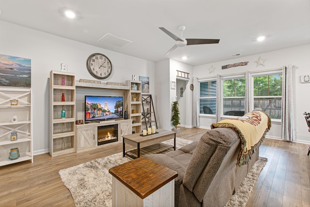 living area featuring a ceiling fan, wood-type flooring, baseboards, a glass covered fireplace, and recessed lighting