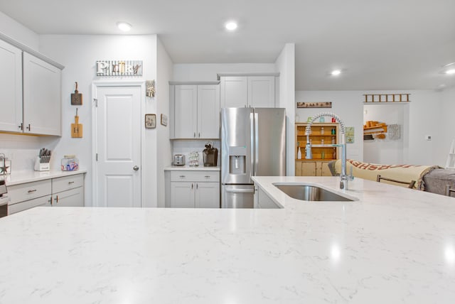 kitchen with stainless steel fridge, light stone counters, a sink, recessed lighting, and backsplash