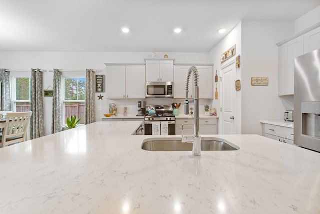 kitchen with stainless steel appliances, a sink, light stone countertops, recessed lighting, and white cabinets