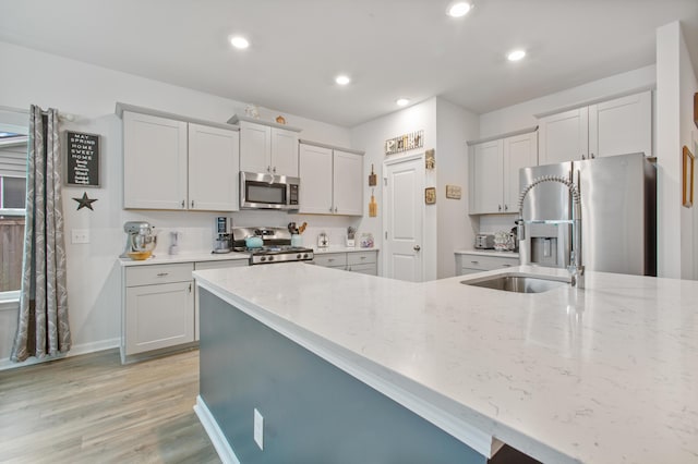 kitchen with appliances with stainless steel finishes, light wood-style flooring, light stone counters, recessed lighting, and a sink