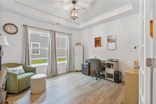 home office featuring a raised ceiling, light wood-type flooring, baseboards, and a chandelier