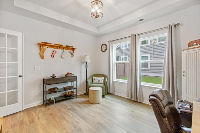 living area featuring a tray ceiling, light wood-style flooring, a chandelier, and baseboards