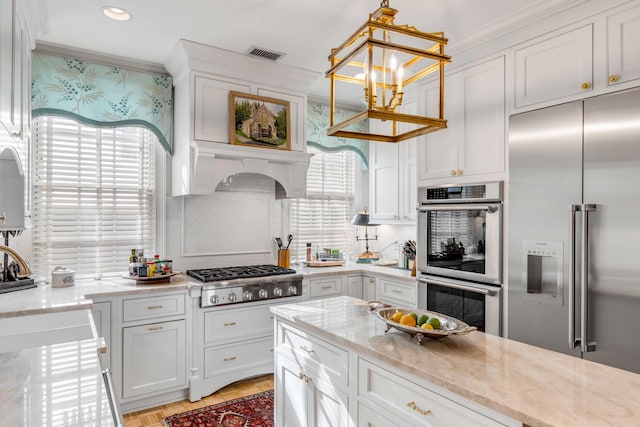 kitchen with light stone countertops, stainless steel appliances, ventilation hood, pendant lighting, and white cabinetry