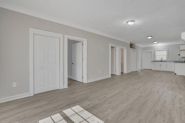 unfurnished living room featuring ornamental molding, sink, and light hardwood / wood-style flooring