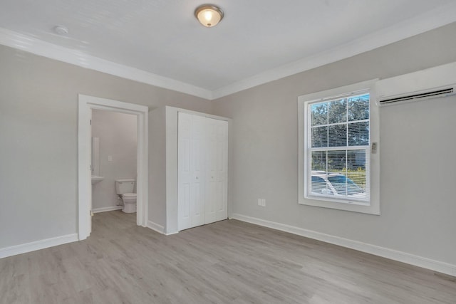 unfurnished bedroom featuring ornamental molding, ensuite bathroom, a wall mounted AC, and light hardwood / wood-style flooring