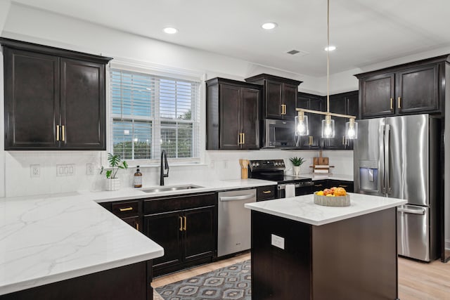 kitchen featuring pendant lighting, sink, appliances with stainless steel finishes, a kitchen island, and light wood-type flooring