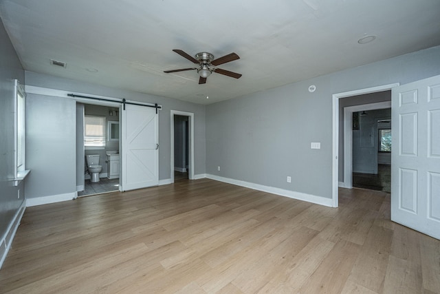 unfurnished room featuring ceiling fan, a barn door, and light wood-type flooring