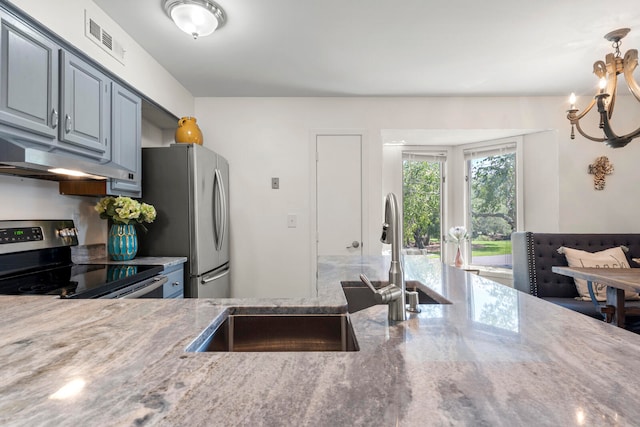 kitchen with light stone countertops, hanging light fixtures, stainless steel appliances, and a notable chandelier