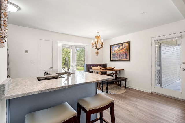 kitchen with decorative light fixtures, sink, light stone counters, light hardwood / wood-style floors, and a breakfast bar