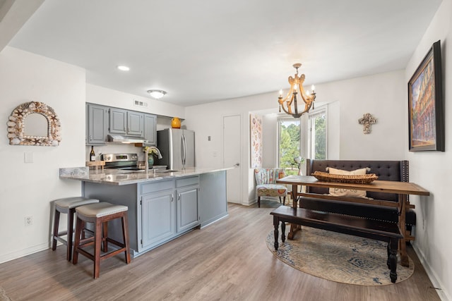 kitchen with stove, light hardwood / wood-style flooring, stainless steel fridge, a breakfast bar, and light stone countertops