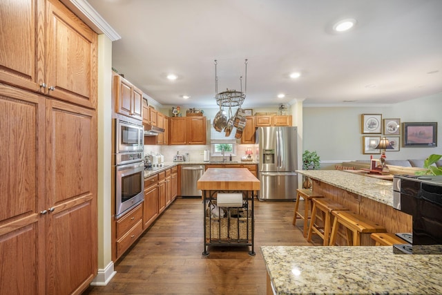 kitchen featuring dark wood-style flooring, ornamental molding, appliances with stainless steel finishes, under cabinet range hood, and recessed lighting
