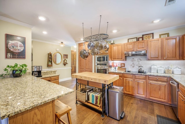 kitchen featuring light stone countertops, crown molding, under cabinet range hood, and appliances with stainless steel finishes