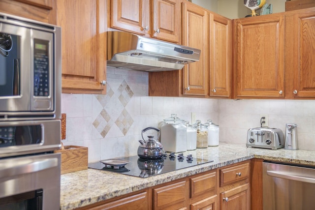 kitchen featuring light stone countertops, under cabinet range hood, tasteful backsplash, and appliances with stainless steel finishes