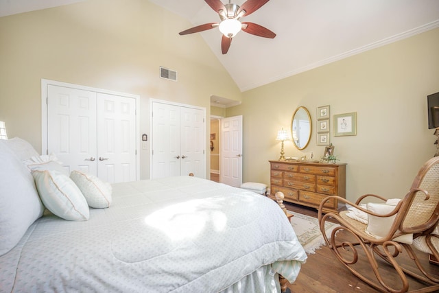 bedroom with visible vents, two closets, a ceiling fan, wood finished floors, and high vaulted ceiling