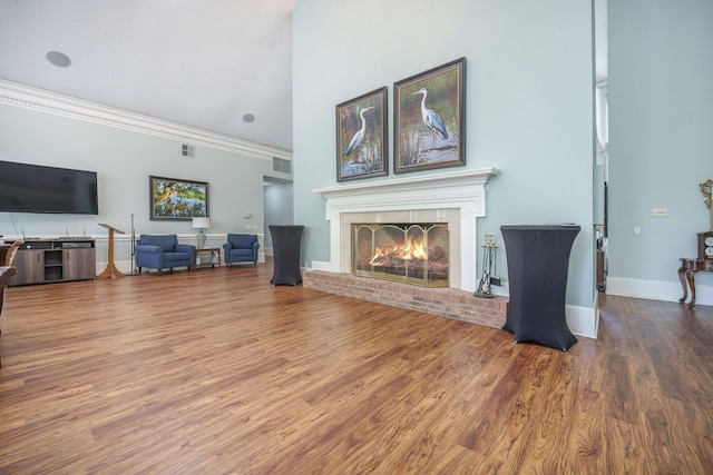living area with a brick fireplace, baseboards, crown molding, and wood finished floors