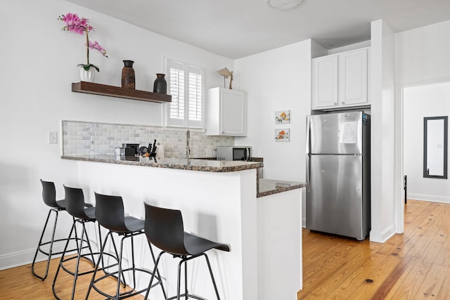 kitchen with a peninsula, white cabinetry, freestanding refrigerator, dark stone counters, and tasteful backsplash