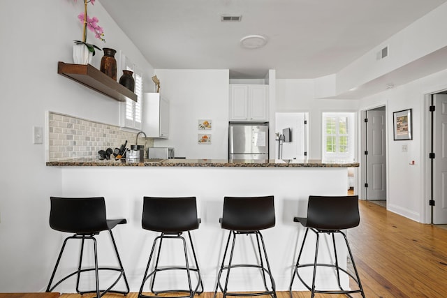 kitchen with visible vents, white cabinetry, dark stone countertops, a peninsula, and stainless steel refrigerator