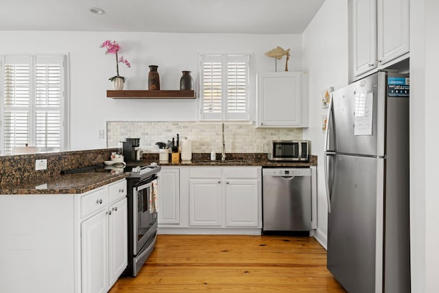 kitchen featuring white cabinets, dark stone countertops, stainless steel appliances, open shelves, and a sink