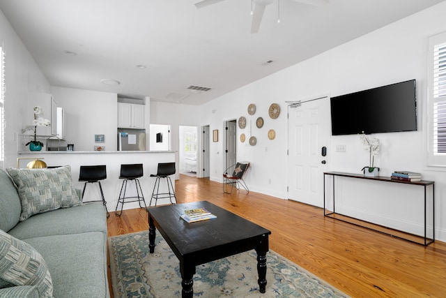 living room with light wood-type flooring, visible vents, ceiling fan, and baseboards